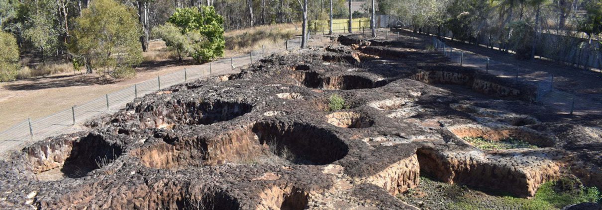 A scenic view of limestone formations at the Carl Werner Ventilation Shaft in Mount Etna Caves National Park, Queensland, Australia. Enclosed by dense greenery and partially fenced, the area features several circular depressions. For those exploring Things To Do Bundaberg, this spot is a hidden gem worth visiting.